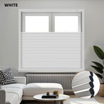 White blackout honeycomb shades covering a window in a living room with a white sofa and decorative items.