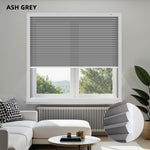 Living room with ash grey light filtering honeycomb shades, white sofa, and a window view.