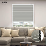 Gray custom size cellular shades in a window with a gray sofa and decorative elements.


